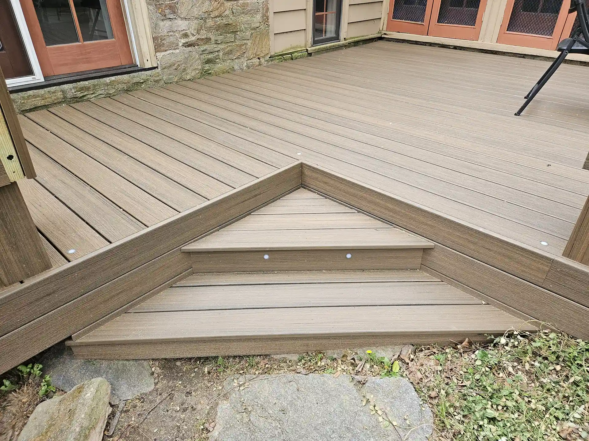 Brown composite two-tone deck with angled picture frame border and flush stairs against a stone house.