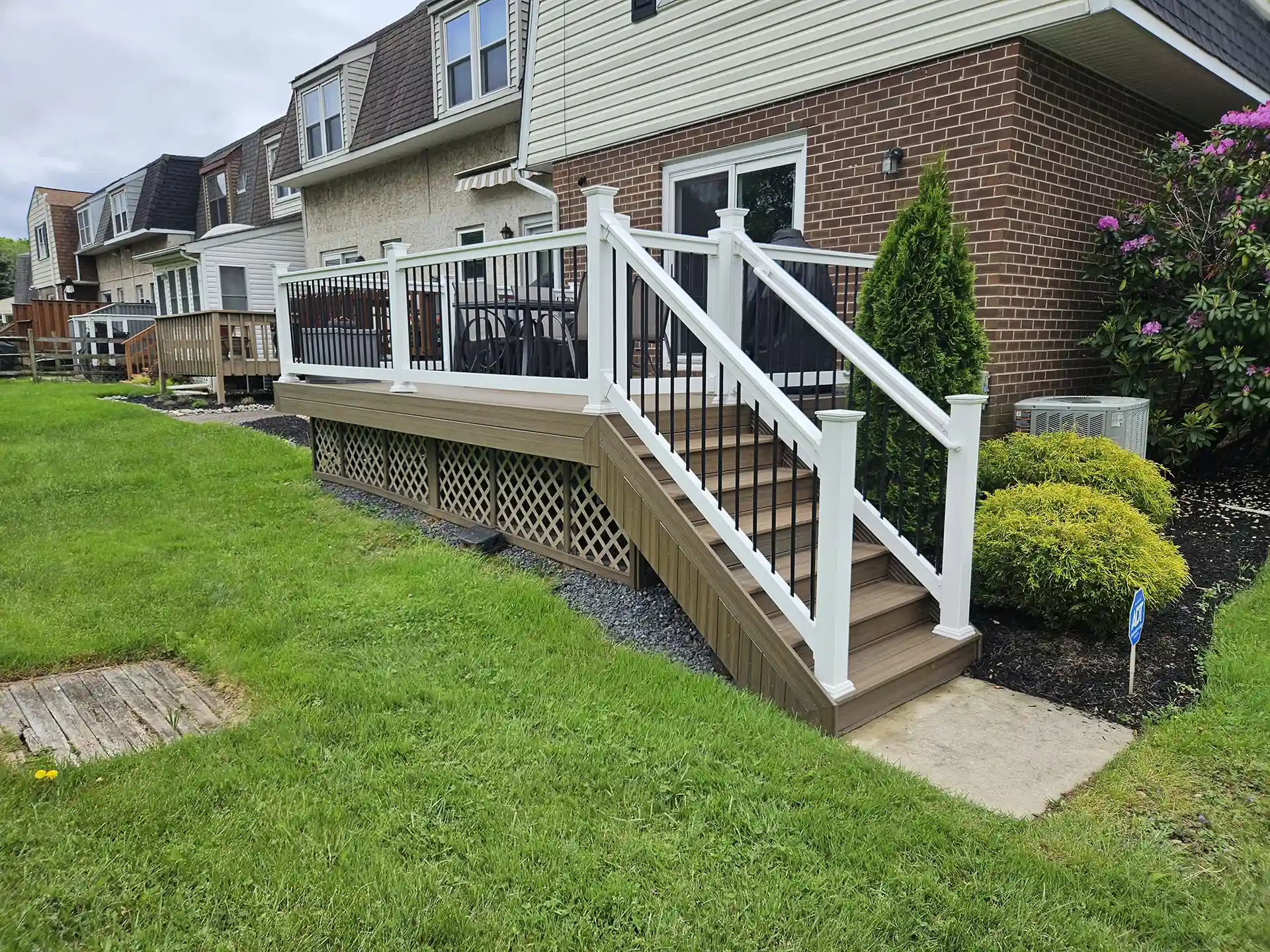 Brown two-tone deck with white posts, black balusters, and lattice skirting on a brick home.