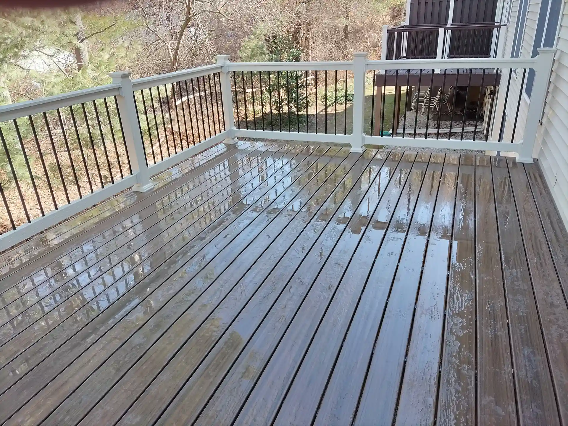 Wet composite deck with white railing and black metal balusters overlooking a wooded backyard. 
