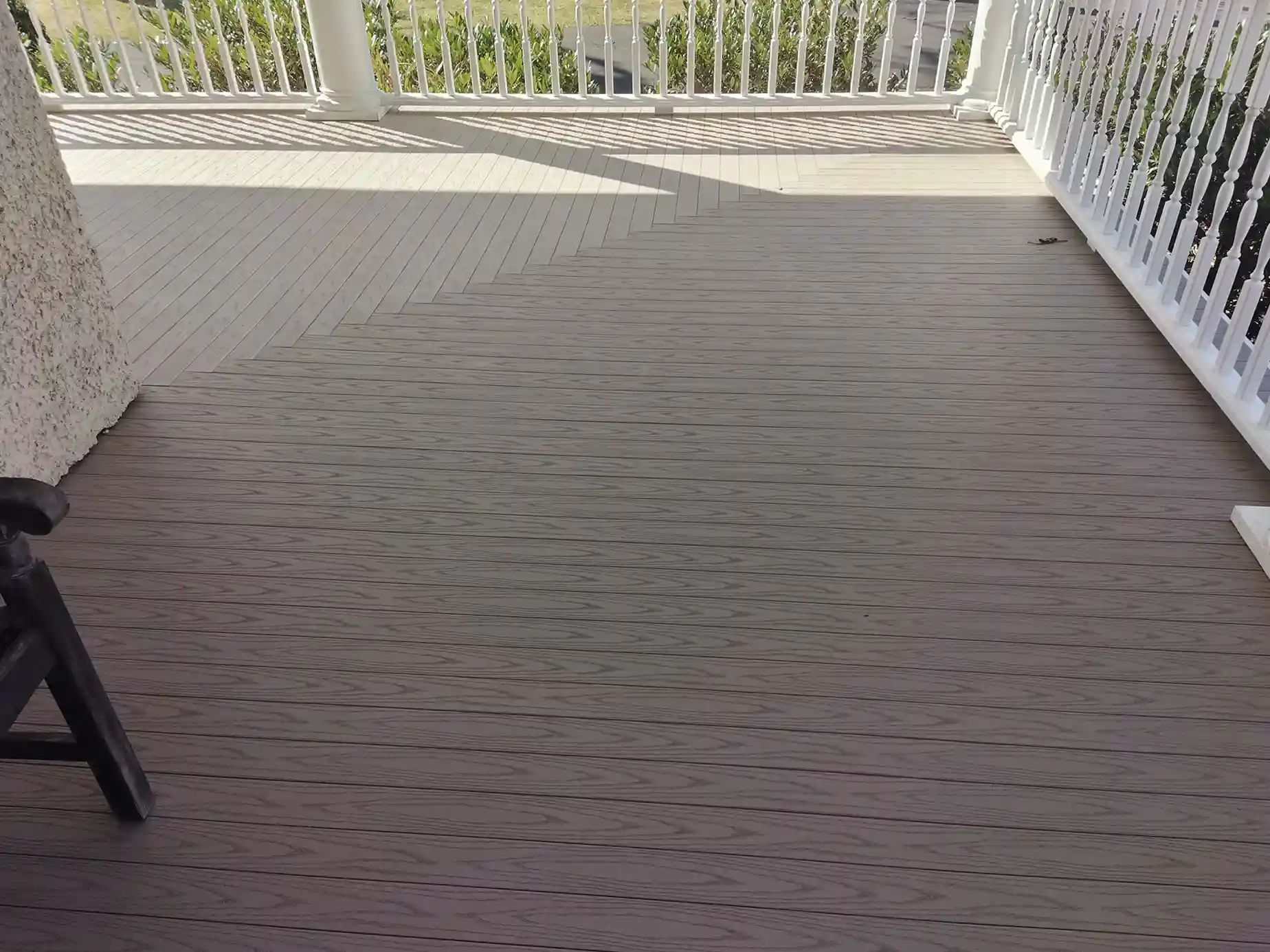 Light-colored composite deck with subtle wood grain texture, white railing, and sunlight casting shadows across the surface. 