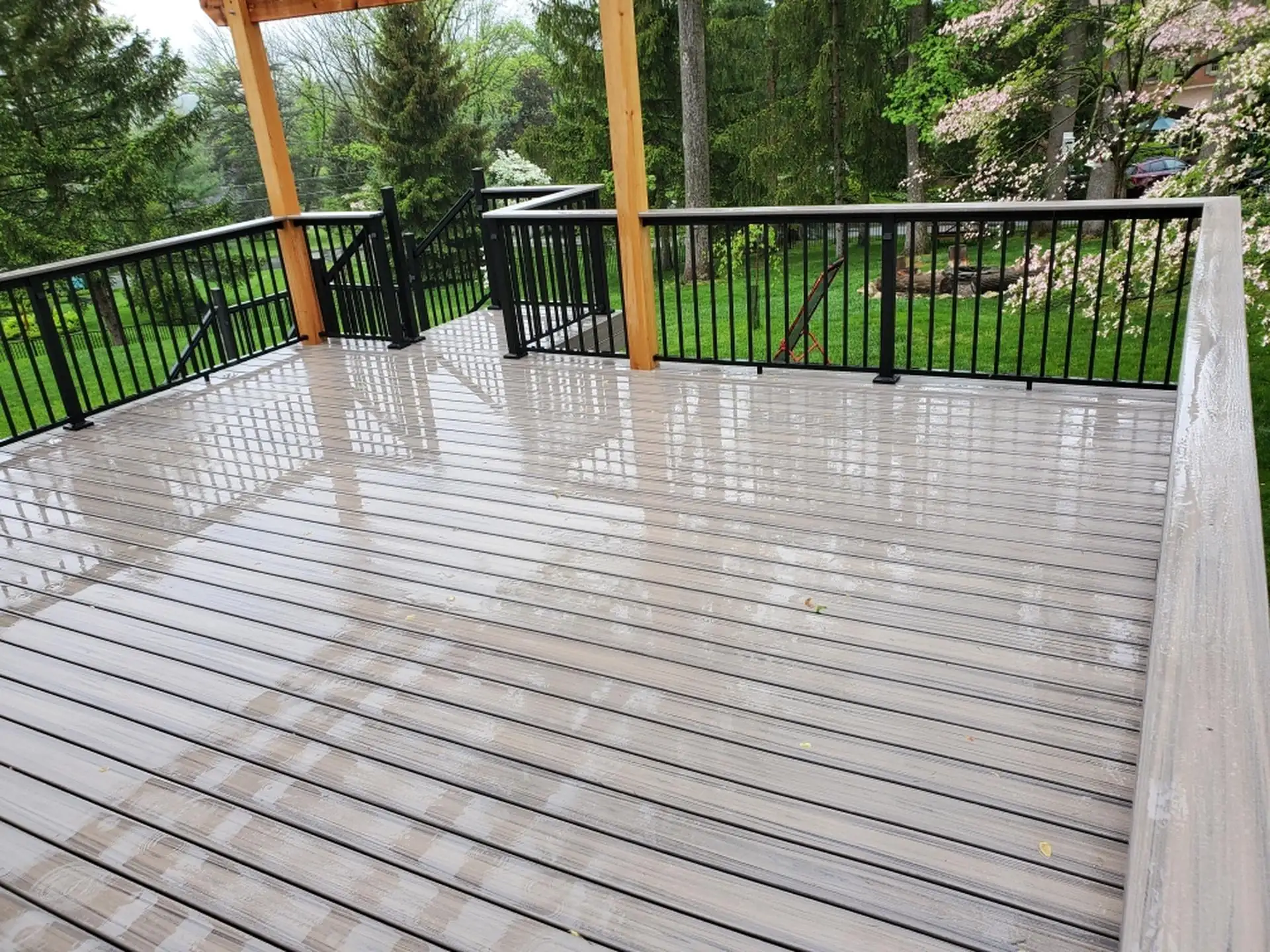 A composite deck with light grey decking boards and black railing. The deck features a modern design with horizontal planks and a set of stairs.