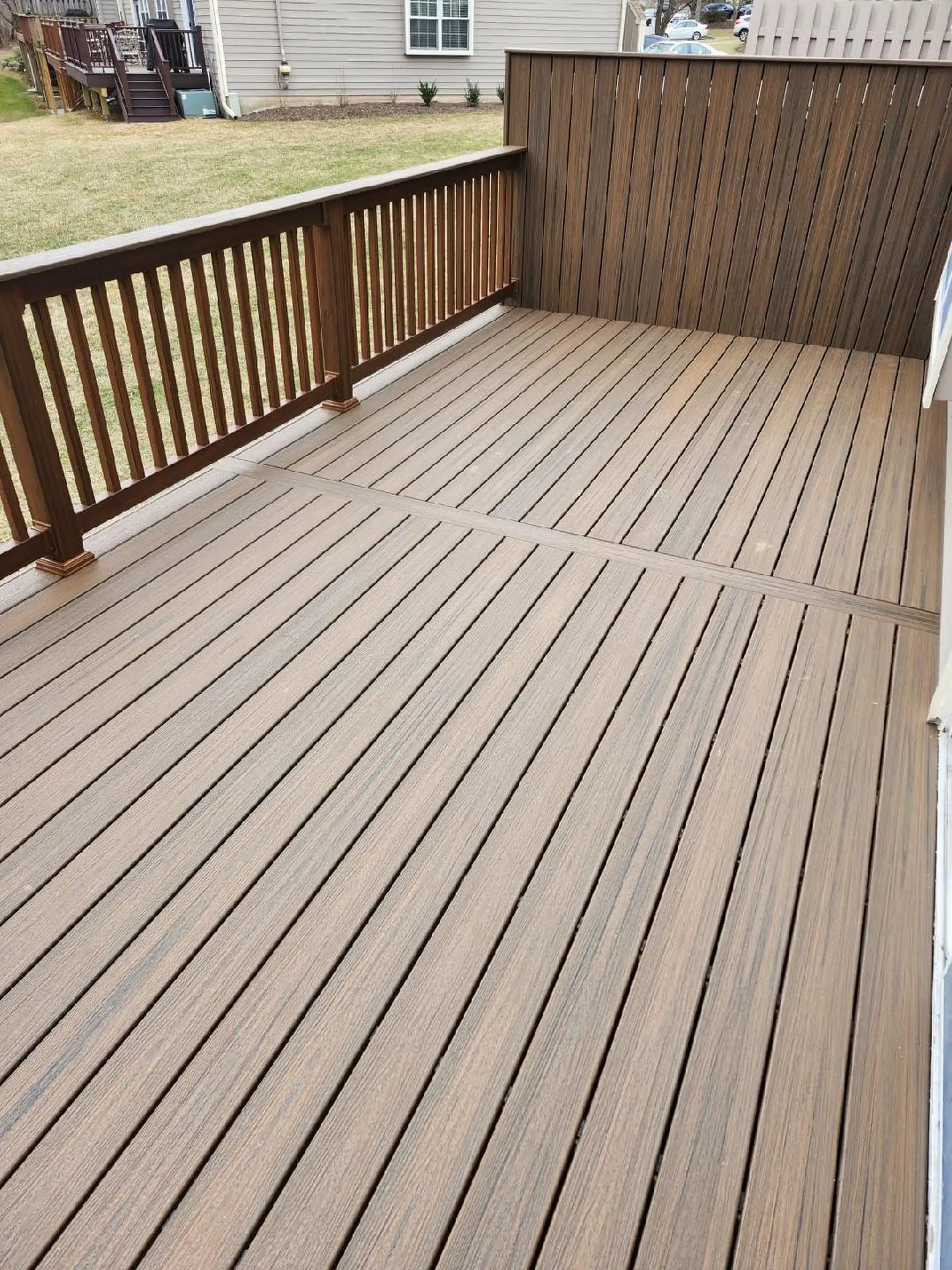 Cedar vs Composite Deck A raised deck with multi-toned composite decking boards. A light wood railing is on the left, and a dark composite privacy wall is on the right.